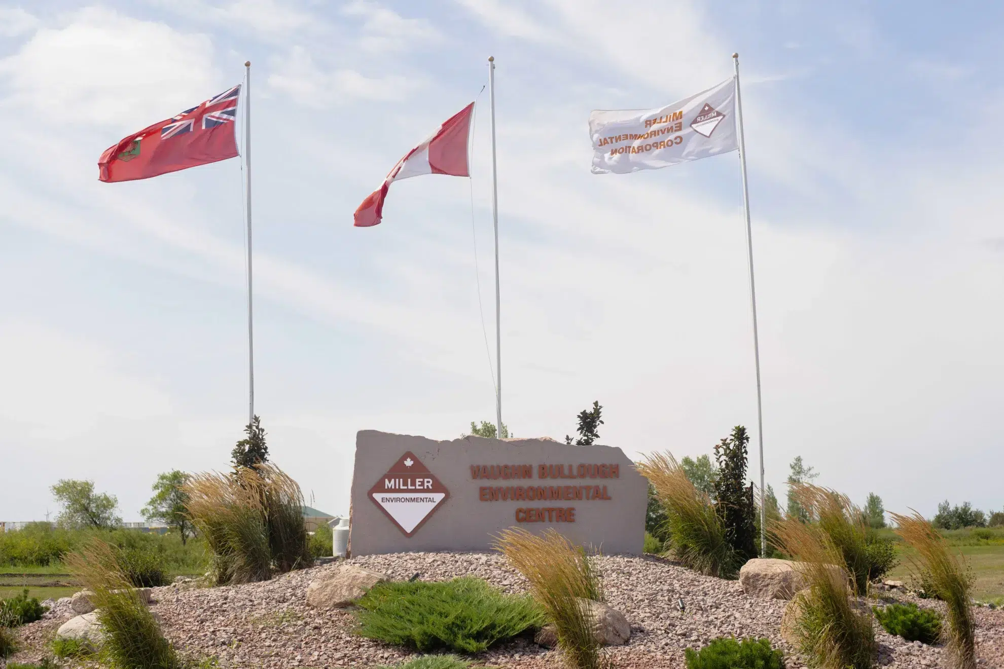 The sign for Miller Environmental's licensed hazardous waste treatment facility, the Vaughn Bullough Environmental Centre. A Manitoba flag, a Canada flag, and a Miller Environmental flag fly above it.