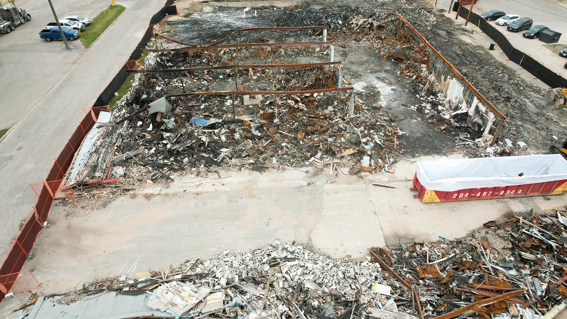 Site of a burned-down strip mall in Steinbach, undergoing asbestos abatement and debris removal. Most of the building has been torn down and debris is being sorted. A lined bin is being used to collect asbestos materials.