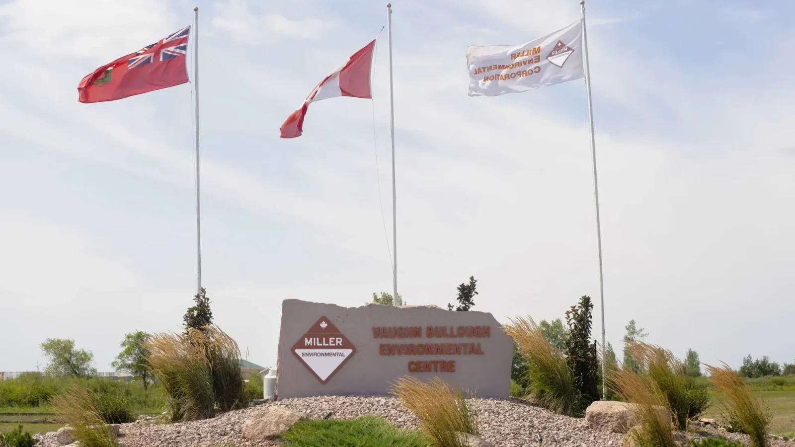 The sign for Miller Environmental's licensed hazardous waste treatment facility, the Vaughn Bullough Environmental Centre. A Manitoba flag, a Canada flag, and a Miller Environmental flag fly above it.